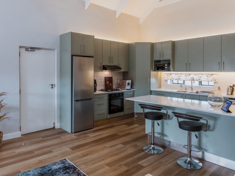 Modern kitchen featuring sage green cabinetry, stone countertops, integrated appliances, and a breakfast island under a vaulted ceiling with ambient lighting.