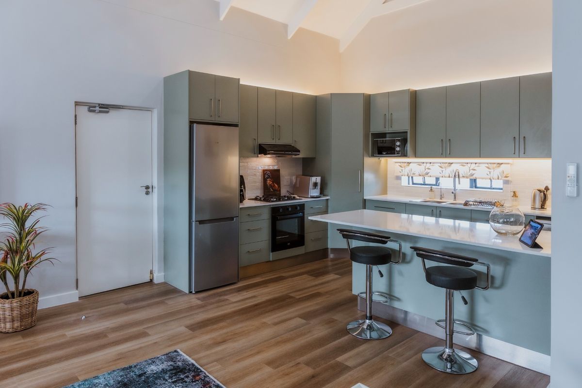 Modern kitchen featuring sage green cabinetry, stone countertops, integrated appliances, and a breakfast island under a vaulted ceiling with ambient lighting.
