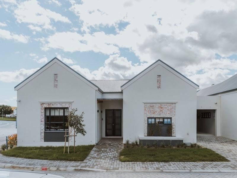 A modern, well-maintained retirement village home featuring a clean white facade, brick accents, and a paved driveway with a covered entrance.