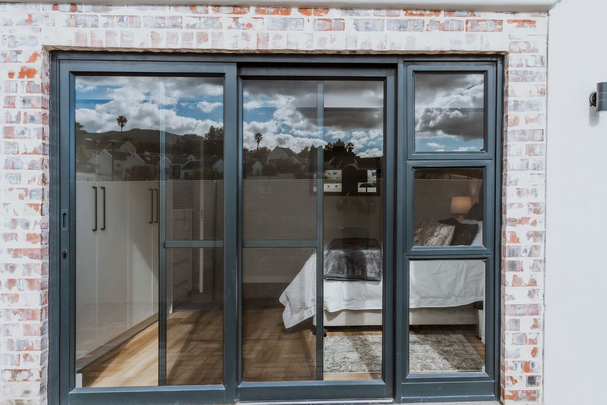 A view of a bedroom interior through a modern sliding glass door set within an exposed brick exterior wall.