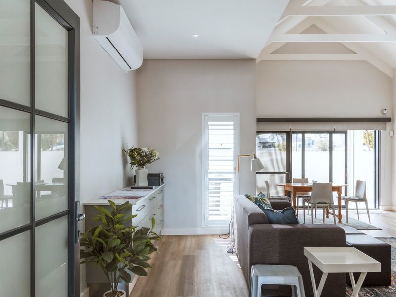 Bright open-plan living area featuring vaulted ceilings with exposed rafters, modern laminate flooring, and seamless access to the outdoor space through sliding glass doors.
