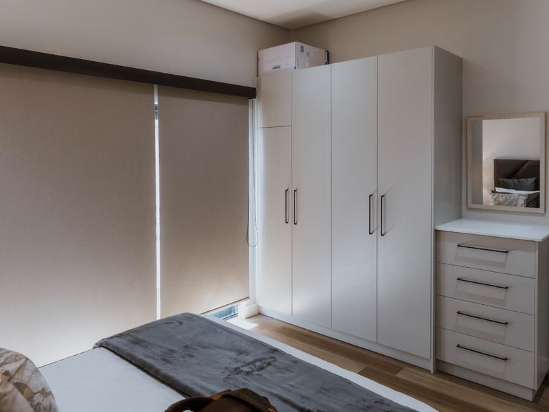 A well-maintained bedroom featuring modern built-in wardrobes, a matching vanity unit, and neutral roller blinds, complemented by clean laminate flooring.