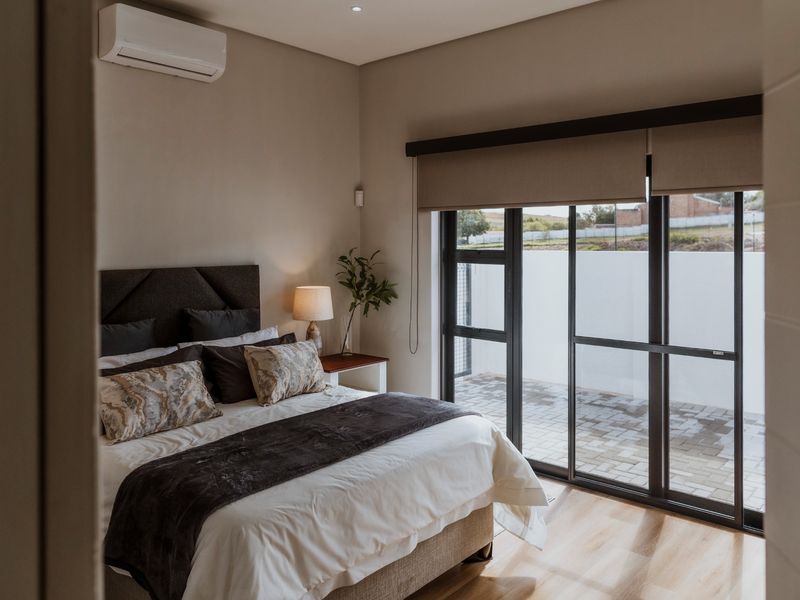 A well-maintained bedroom featuring modern laminate flooring, a split-system air conditioner, and large sliding glass doors providing access to an outdoor patio area.