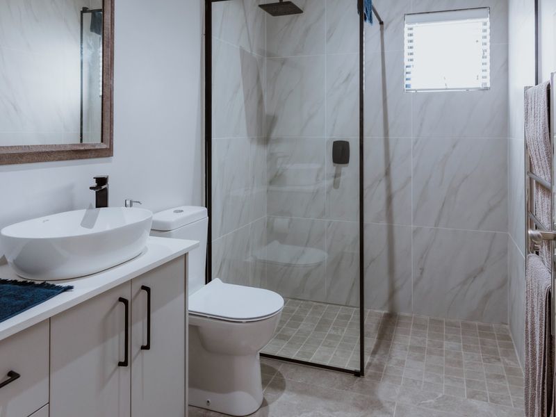 Modern bathroom featuring a sleek vanity with vessel sink, walk-in shower with marble-look tiling, and a heated towel rail.