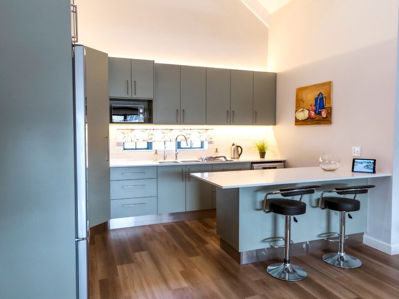Modern kitchen featuring sage green cabinetry, stone countertops, integrated microwave, and a breakfast bar with under-cabinet lighting in a bright, open-plan setting.