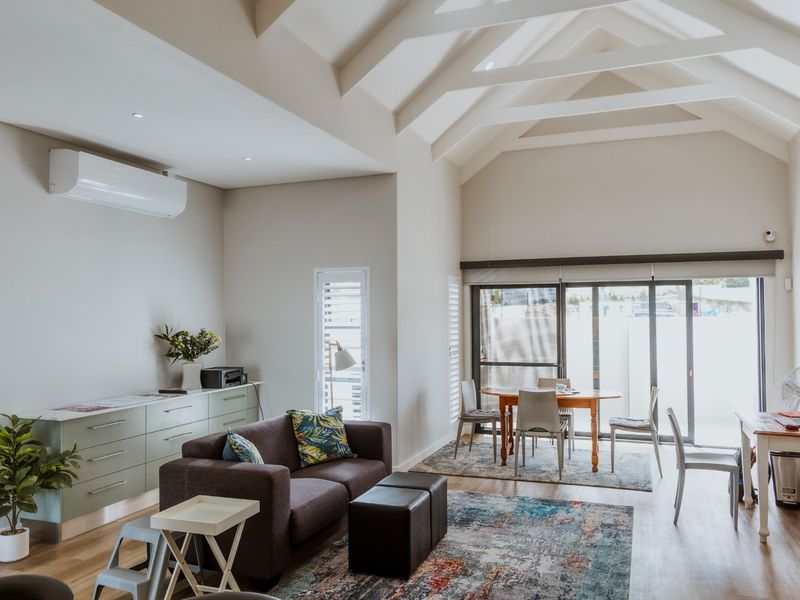 Spacious open-plan living and dining area featuring high vaulted ceilings with exposed rafters, modern laminate flooring, and large sliding doors leading to the patio.