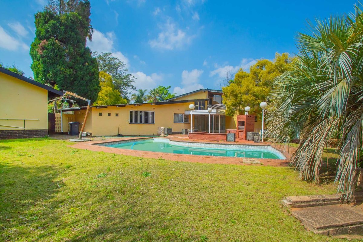 Rear exterior view featuring a swimming pool, brick-built braai area, and established garden space with paved surrounds.