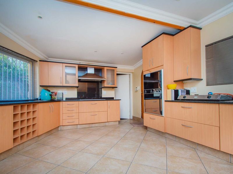Spacious kitchen featuring light wood-finish cabinetry, granite countertops, built-in oven, extractor fan, and tiled flooring with ample storage space.