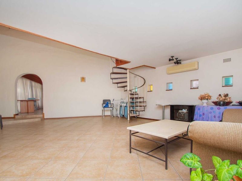 Spacious living area featuring a central spiral staircase, tiled flooring, and an arched entryway leading to an adjacent room.
