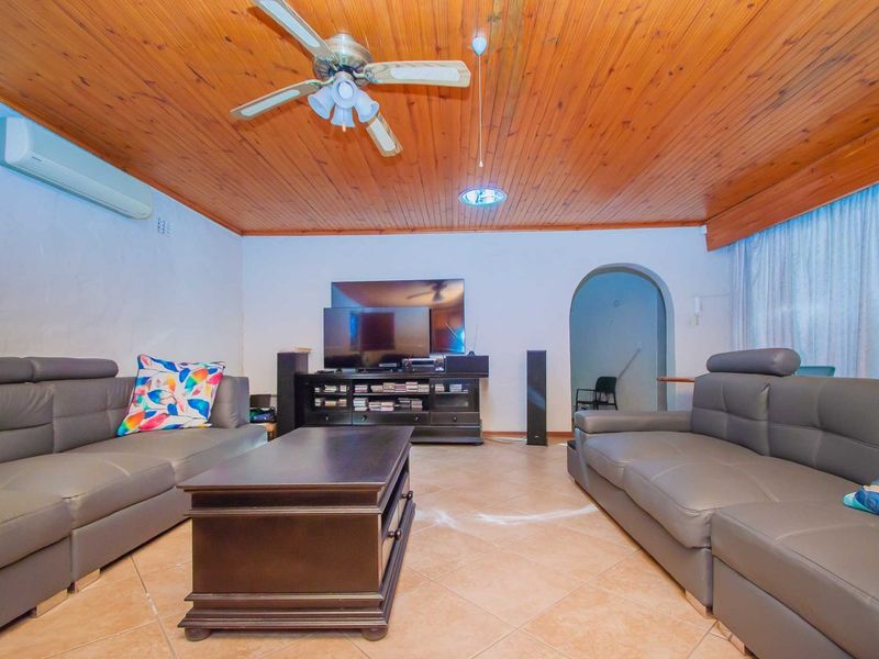 A living room featuring a timber tongue and groove ceiling, ceramic floor tiles, a ceiling fan, and a split system air conditioner.