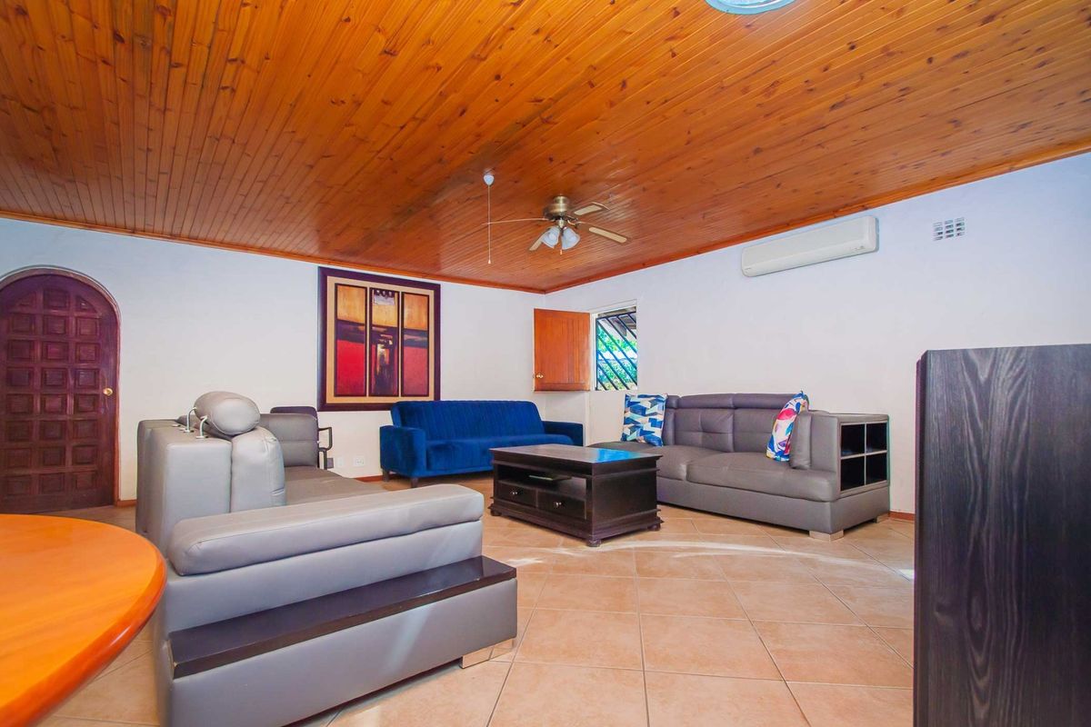 Spacious living room featuring a warm timber-clad ceiling, tiled flooring, and a split-system air conditioner for climate control.