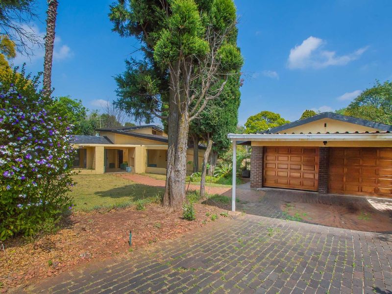 Front view of the property featuring a double garage, brick driveway, and a covered entrance walkway set within a mature garden.