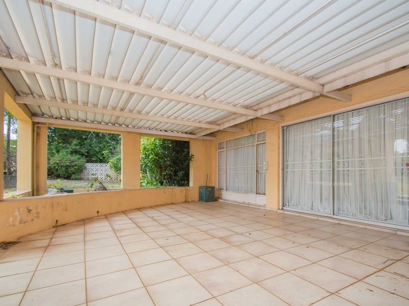 A spacious covered patio featuring tiled flooring, a corrugated roof, and sliding glass doors providing access to the interior living area.