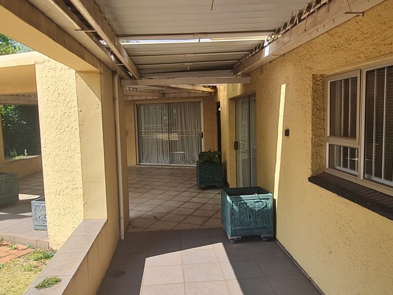A covered outdoor patio area featuring tiled flooring, sliding glass door access, and textured exterior walls, providing a functional transition space to the garden.
