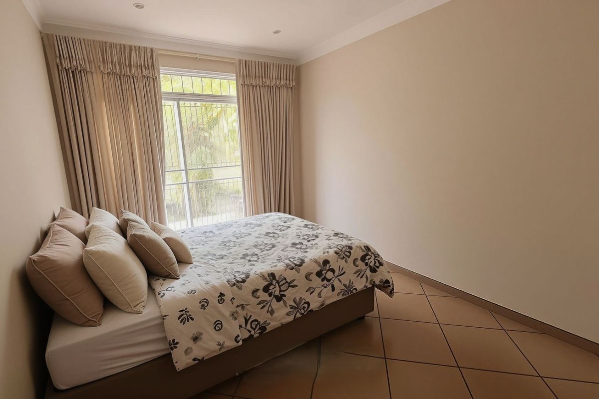 A well-maintained bedroom featuring neutral wall tones, tiled flooring, and a sliding glass door with security gate providing access to the exterior.