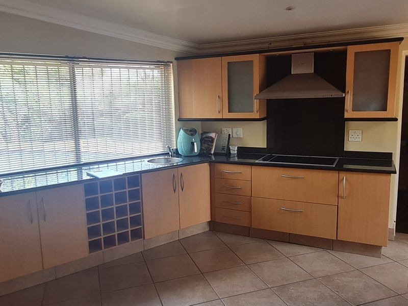 Functional kitchen featuring light wood cabinetry, dark granite countertops, integrated hob with extractor fan, and tiled flooring.