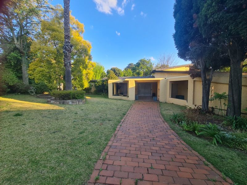 A rear view of the property featuring a brick paved walkway leading to a covered patio area set within a mature garden.