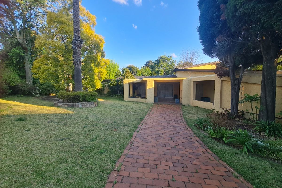 A rear view of the property featuring a brick paved walkway leading to a covered patio area set within a mature garden.