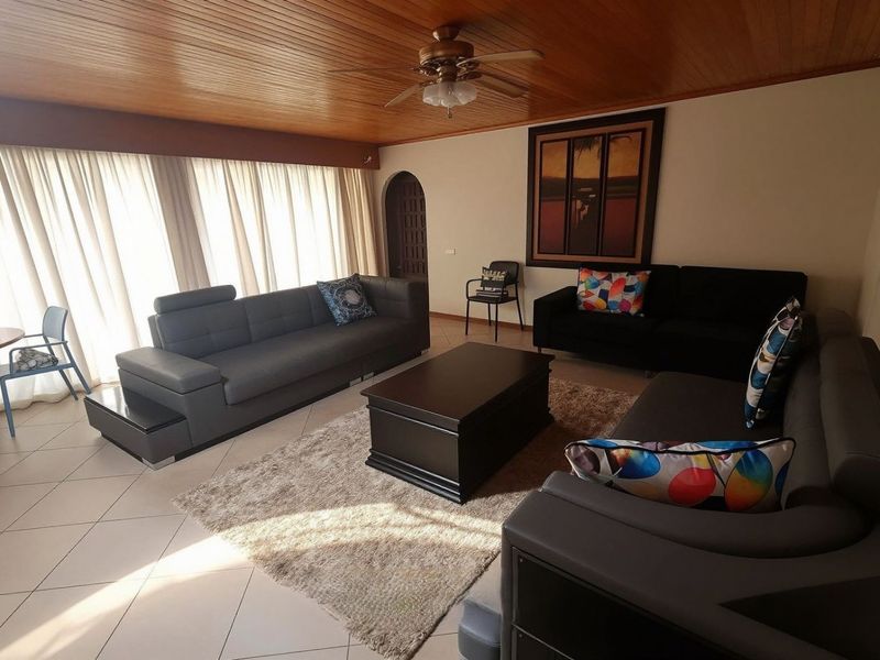 Spacious living room featuring a warm timber-paneled ceiling, ceiling fan, and neutral tiled flooring with an arched doorway leading to adjacent areas.