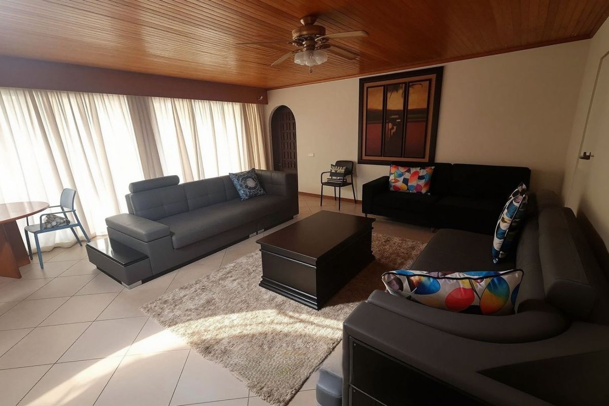 Spacious living room featuring a warm timber-paneled ceiling, ceiling fan, and neutral tiled flooring with an arched doorway leading to adjacent areas.