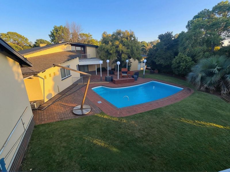 An elevated view of a private backyard featuring a swimming pool, brick-paved patio area, and established garden surroundings.