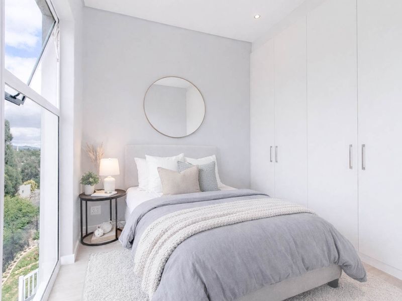A bright and modern bedroom featuring floor-to-ceiling windows with natural light and ample built-in cupboard storage.
