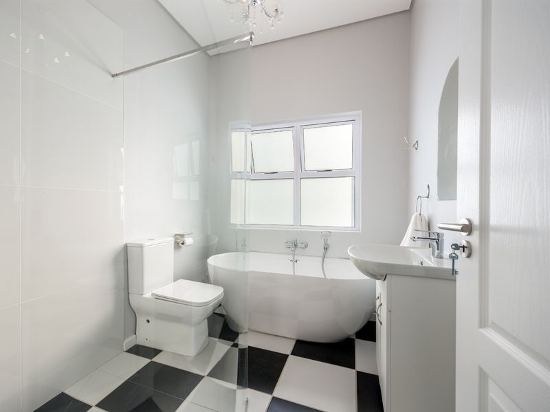 A modern, well-maintained bathroom featuring a freestanding bathtub, a sleek vanity basin, and a glass shower screen with a classic black and white tiled floor.