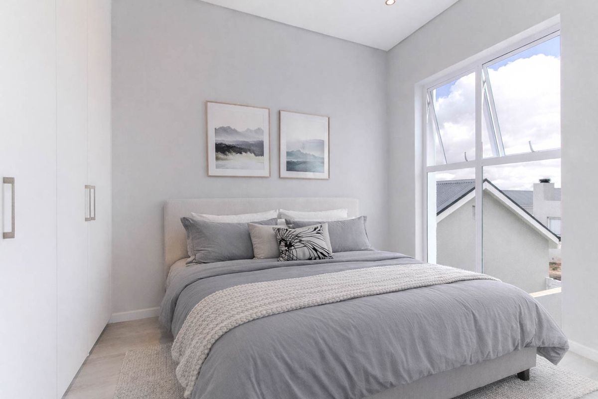 A modern, well-lit bedroom featuring built-in cupboards, neutral finishes, and a large window providing natural light and a view of the surrounding area.