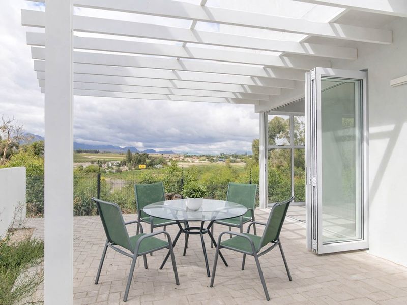 Covered patio area featuring a white pergola structure, paved flooring, and bi-fold doors providing seamless indoor-outdoor flow with scenic landscape views.