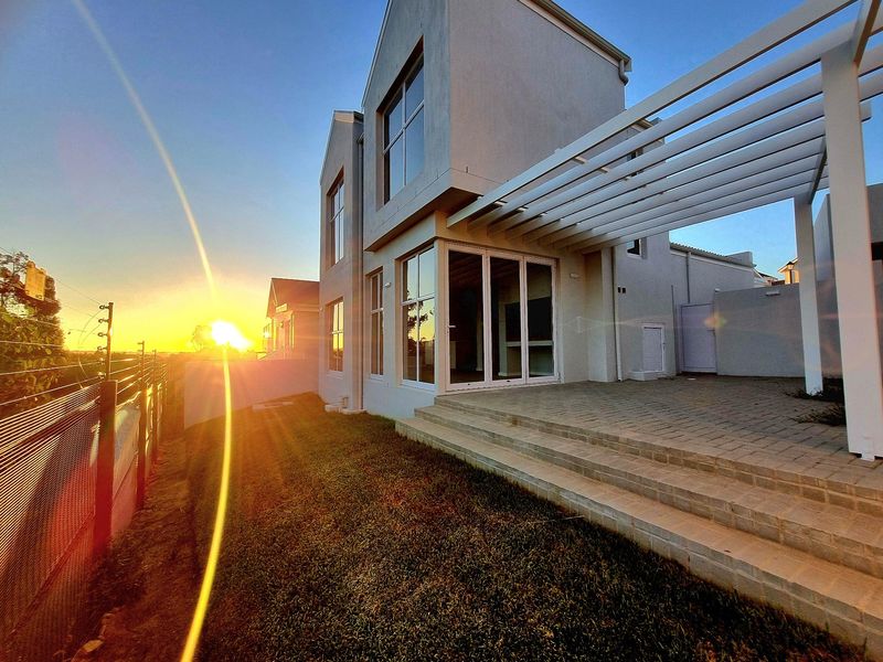 Rear view of a modern two-story house featuring a paved patio with a pergola, large sliding glass doors, and a landscaped garden area.