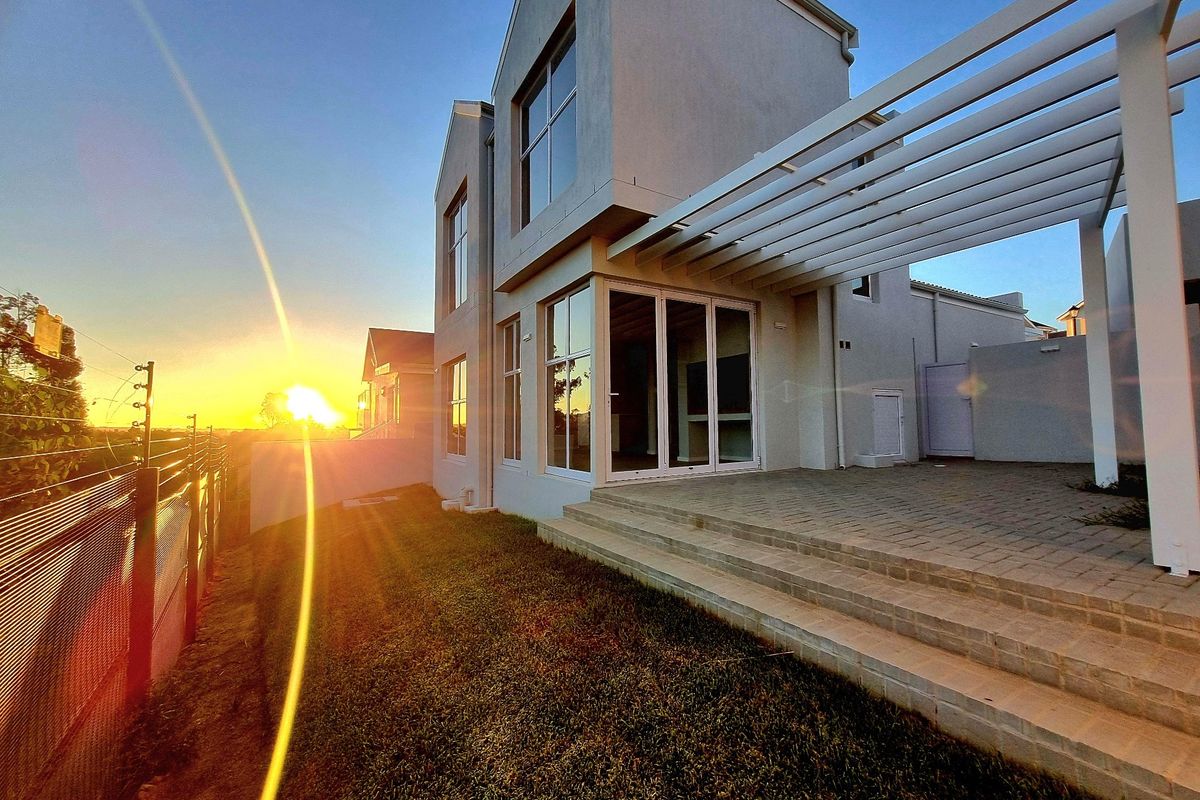 Rear view of a modern two-story house featuring a paved patio with a pergola, large sliding glass doors, and a landscaped garden area.