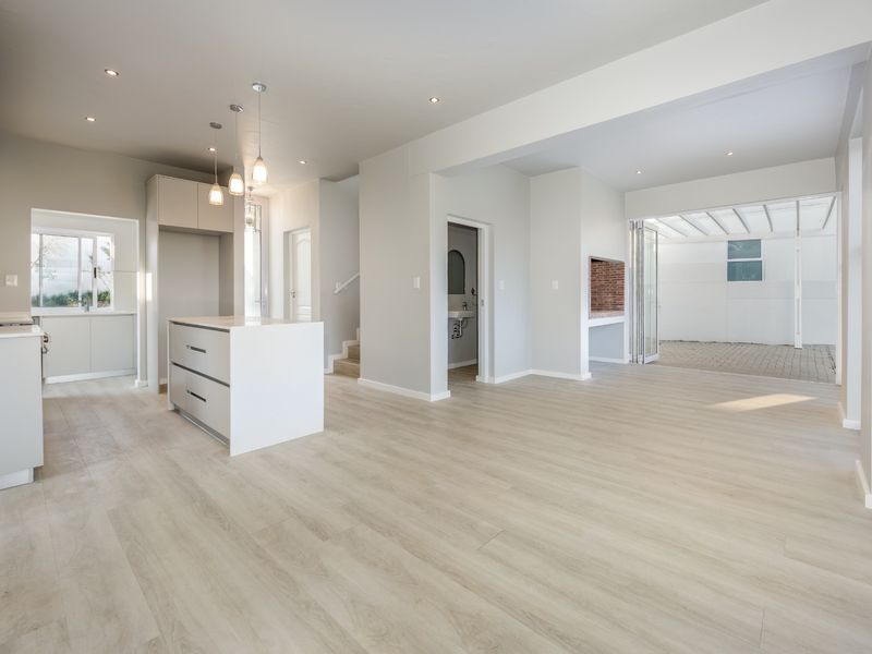 Spacious open-plan living area featuring a modern kitchen island, recessed lighting, laminate flooring, and a built-in brick fireplace leading to an outdoor patio.