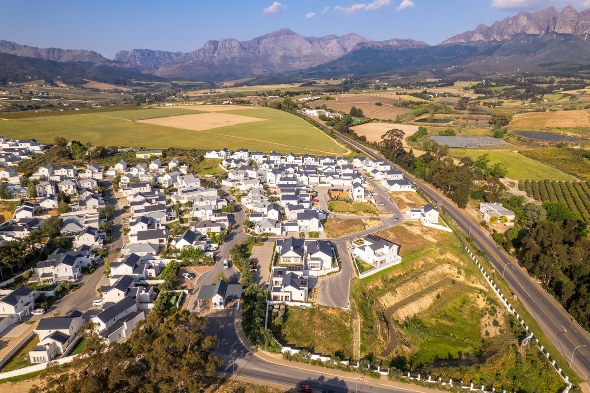 Aerial view of a residential estate featuring modern homes, paved internal roads, and scenic mountain views in the surrounding landscape.