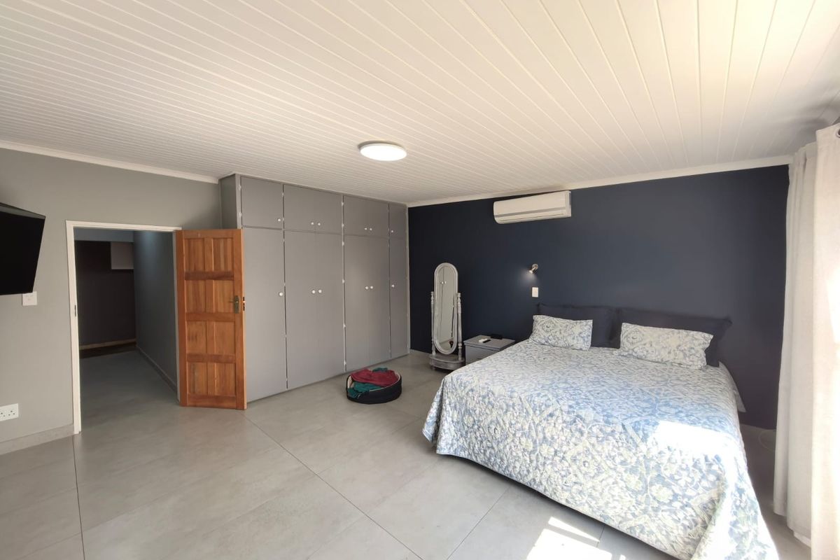 Spacious bedroom featuring large built-in cupboards, tiled flooring, a tongue and groove ceiling, and a wall-mounted air conditioning unit.