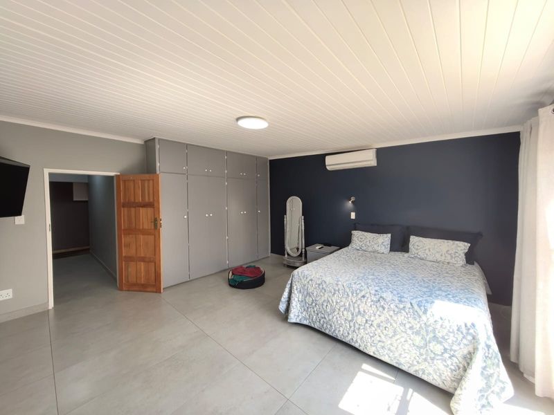 Spacious bedroom featuring large built-in cupboards, tiled flooring, a tongue and groove ceiling, and a wall-mounted air conditioning unit.