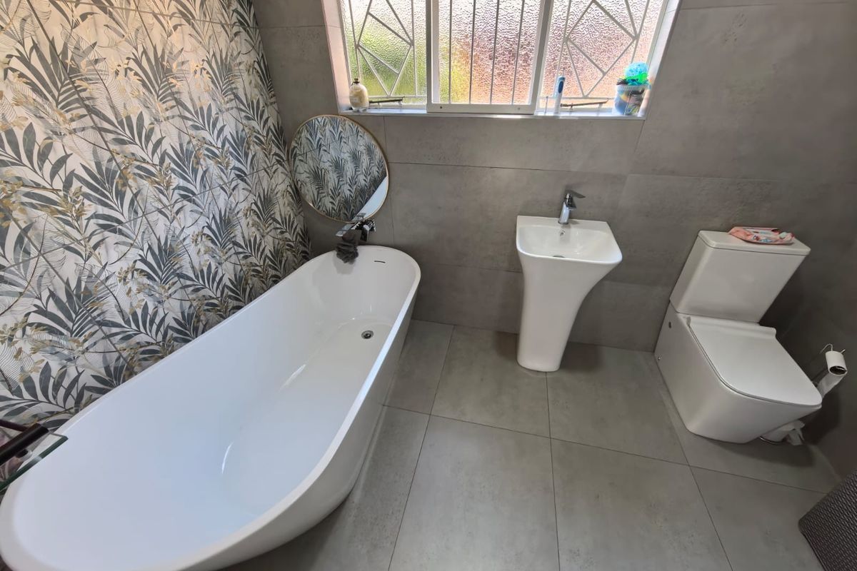 Modern bathroom featuring a sleek freestanding bathtub, pedestal basin, toilet, and a stylish patterned feature wall with large-format grey floor tiles.