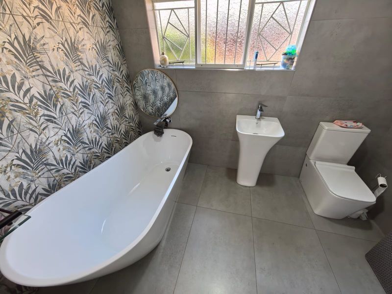 Modern bathroom featuring a sleek freestanding bathtub, pedestal basin, toilet, and a stylish patterned feature wall with large-format grey floor tiles.