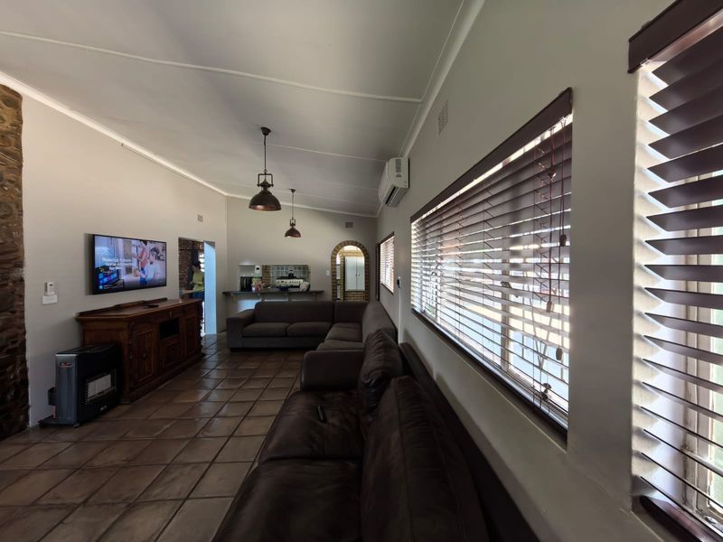 Spacious living area featuring tiled flooring, a stone feature wall, split-system air conditioning, and large windows with venetian blinds.