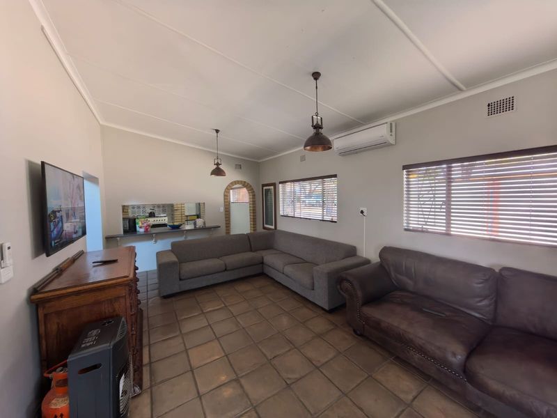 A spacious living room featuring tiled flooring, split-system air conditioning, and pendant lighting, with an adjacent archway leading to a secondary area.
