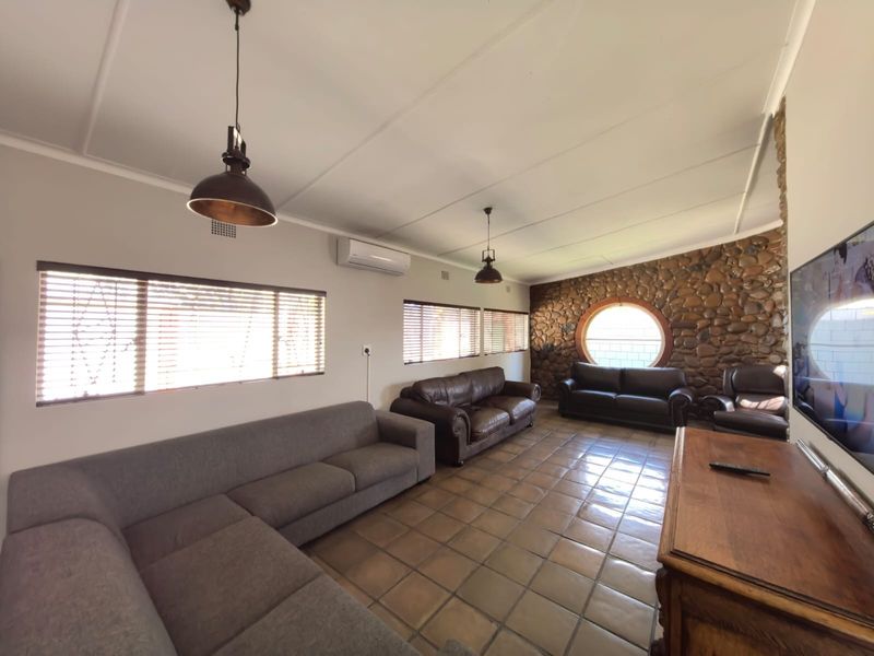Spacious living room featuring a distinctive stone accent wall, circular window, ceramic tile flooring, and split-system air conditioning for climate control.