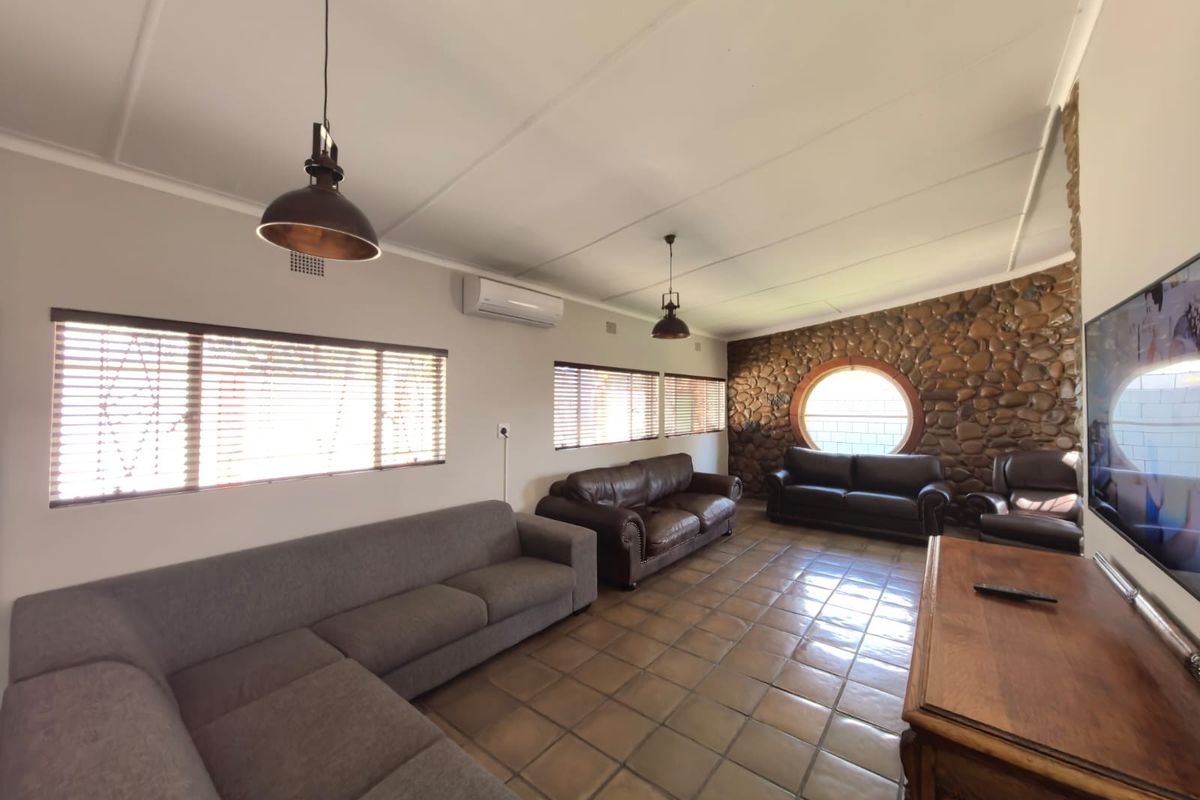 Spacious living room featuring a distinctive stone accent wall, circular window, ceramic tile flooring, and split-system air conditioning for climate control.