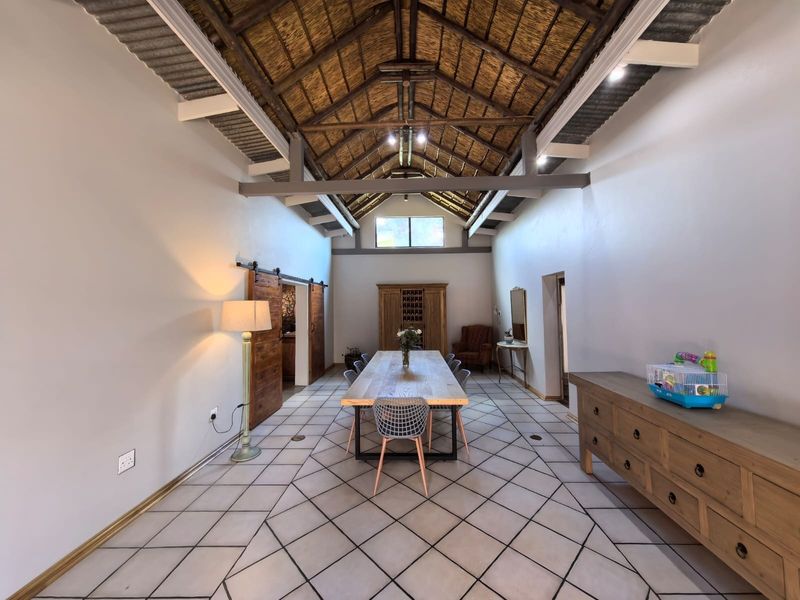 Spacious dining room featuring a high vaulted ceiling with exposed thatch and timber trusses, complemented by tiled flooring and rustic sliding barn doors.
