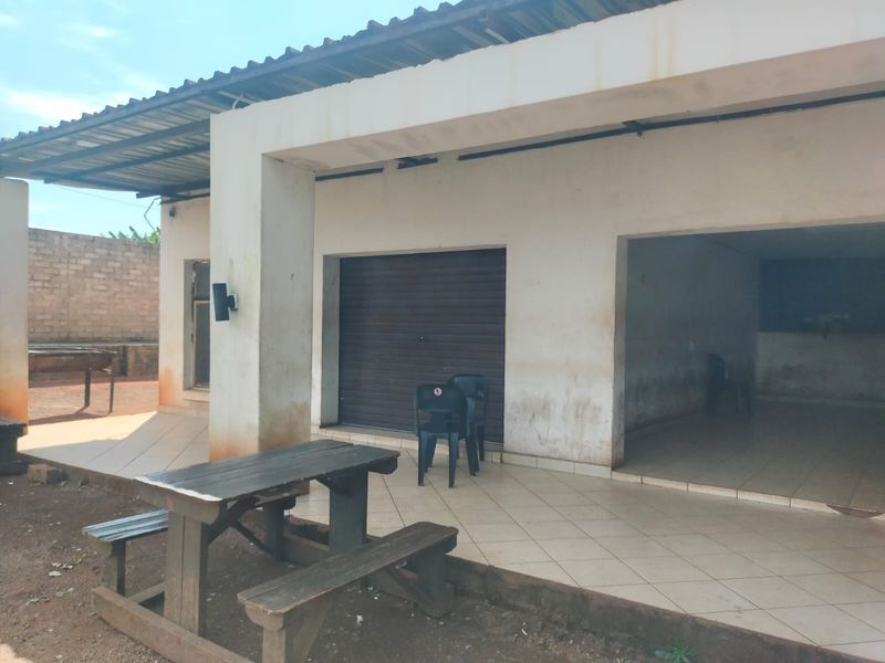 Covered outdoor patio area featuring tiled flooring, concrete structural pillars, and a secure roller shutter door entrance.