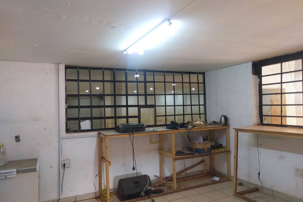 A utility or workspace area featuring tiled floors, security bars on windows, and basic lighting, currently in need of cosmetic refurbishment and wall repairs.