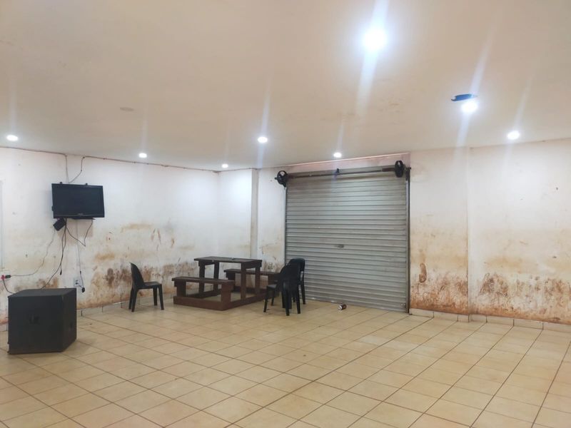 Open plan commercial space featuring tiled flooring, recessed lighting, and a secure roller shutter door, currently showing significant wall wear and surface damage.