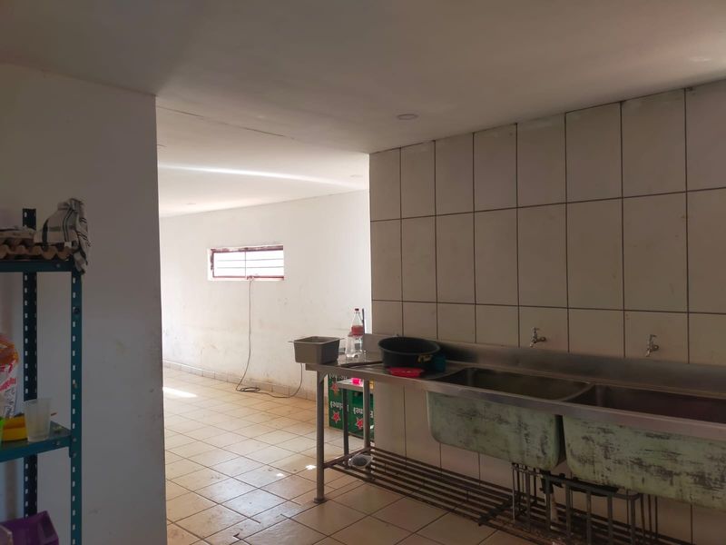 A functional scullery or wash-up area featuring a stainless steel double sink, tiled splashback, and tiled flooring, suitable for commercial kitchen preparation.
