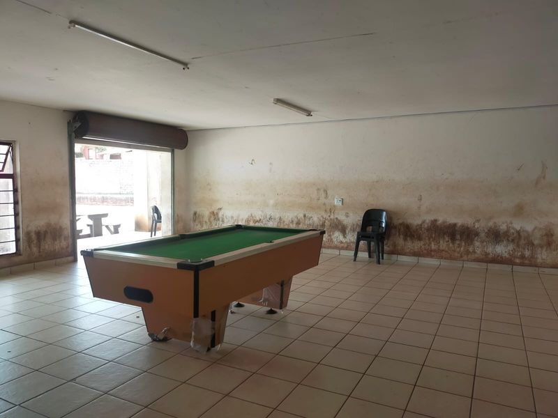 Open plan commercial space featuring tiled flooring and a roller shutter door, currently showing significant wall staining and signs of moisture damage.