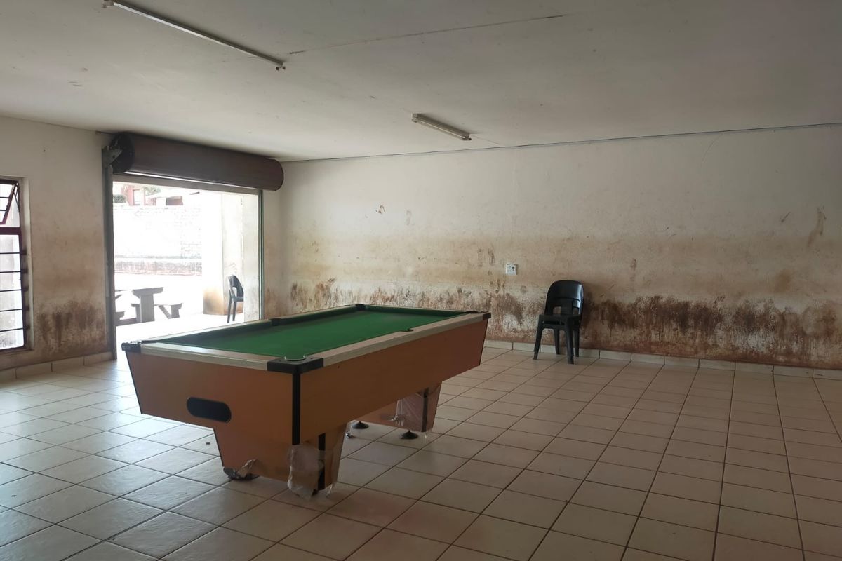 Open plan commercial space featuring tiled flooring and a roller shutter door, currently showing significant wall staining and signs of moisture damage.