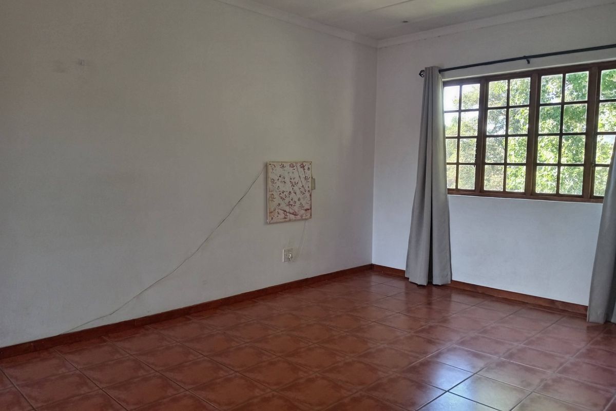 An empty living room featuring terracotta-style tiled flooring and large wooden-framed windows, providing a blank canvas for interior design.