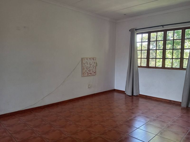 An empty living room featuring terracotta-style tiled flooring and large wooden-framed windows, providing a blank canvas for interior design.